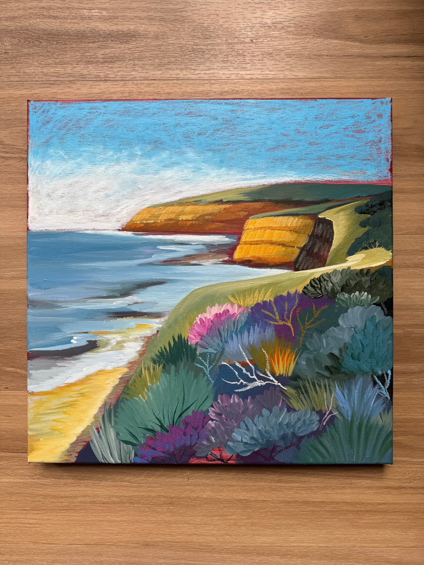 Jan Juc at Day by Lauren Danger, a colourful seascape original painting inspired by the Surf Coast location of Jan Juc near Torquay, Victoria, Australia. Painting is sitting on a wooden background for scale.