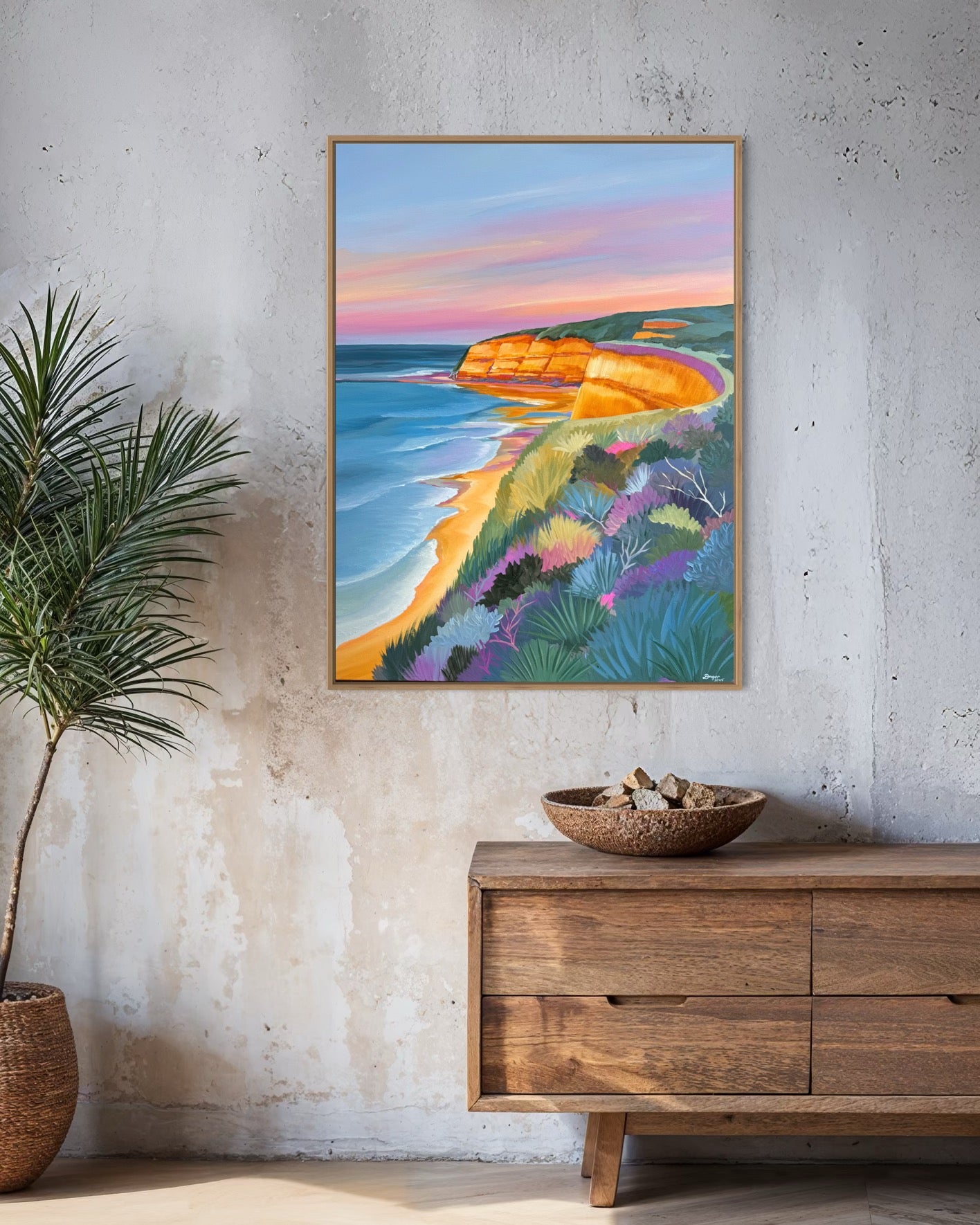 A close up of the colourful artwork Jan Juc at Sunrise by Lauren Danger.  The image has vibrant colours of the cliffs sea and vegetation in Jan Juc in acrylic.  The painting is displayed in a living room above a sideboard, framed in raw oak